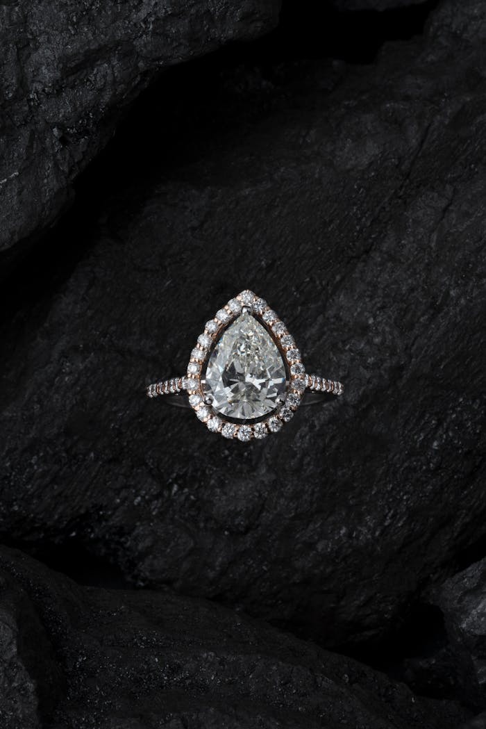 services-02 Stunning teardrop diamond ring surrounded by smaller stones on a textured dark background.